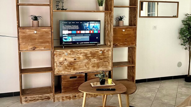 A living room with a wooden entertainment unit, a television, a round coffee table, and a sofa. - Cosy, modern studio - Gard (Saint-Ambroix)