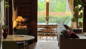 Un intérieur chaleureux avec un coin repas, un canapé et une vue sur la verdure environnante.