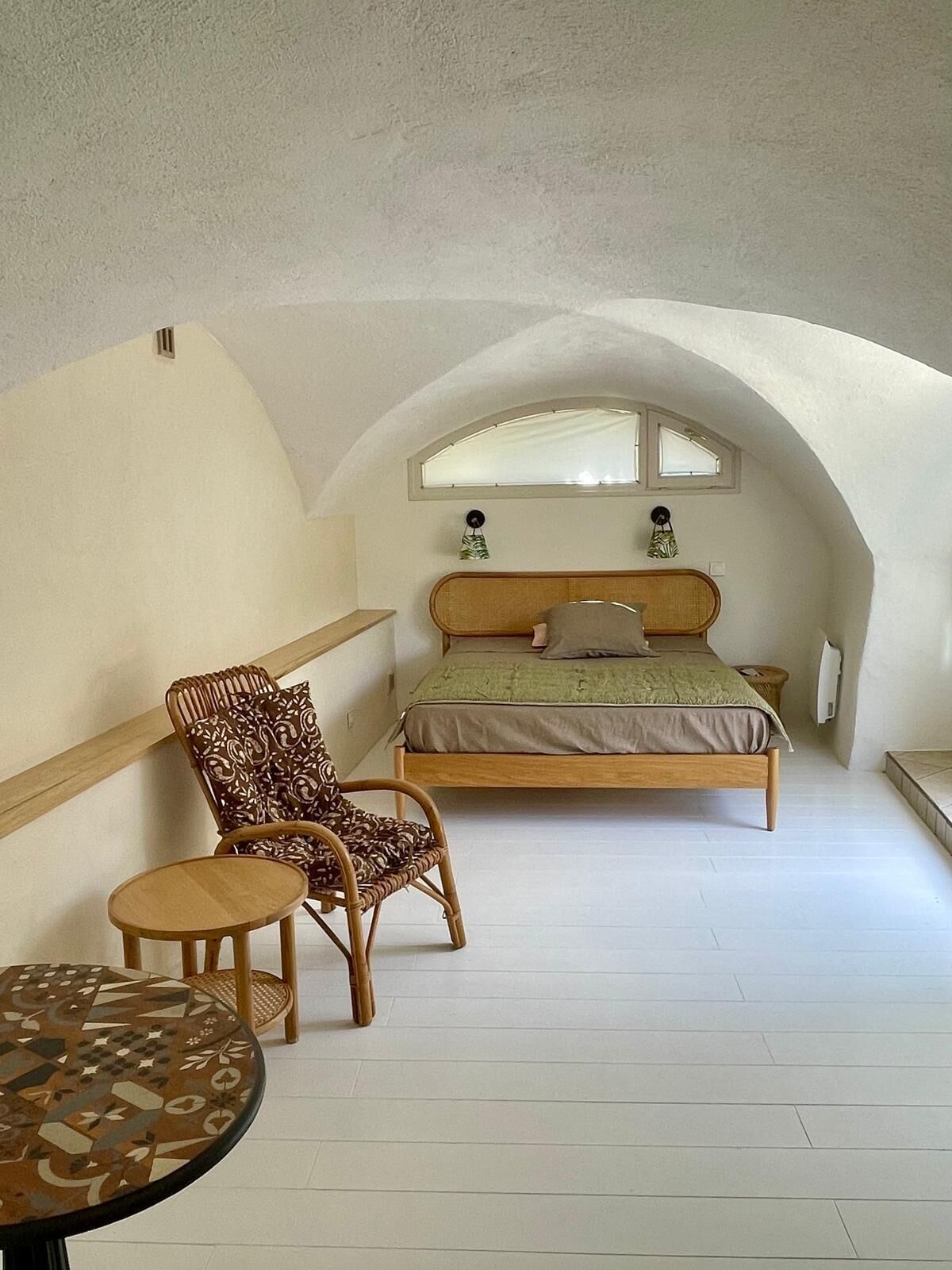 Un dormitorio con cama, una silla, una mesita y una ventana.