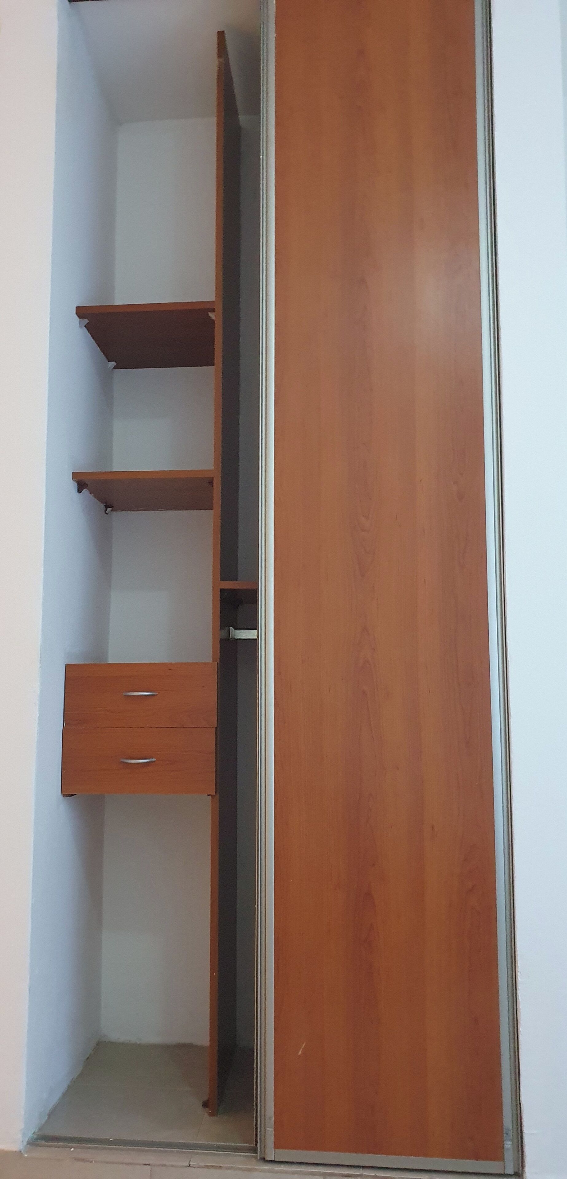 A wooden wardrobe with a mirrored door, a shelf, and a drawer.