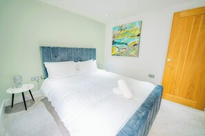 A neatly made bed with white linens, a blue headboard, and a wooden door. - Central Gloucestershire Flat 1 Bedroom  Sleeps 6 (Gloucestershire)