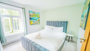 A bedroom with a large bed, a window, a radiator, a small table, and a painting on the wall. - Central Gloucestershire Flat 1 Bedroom  Sleeps 6 (Gloucestershire)