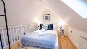 A bedroom with a sloped ceiling, a bed with a blue blanket, two bedside tables with lamps, and a framed picture on the wall. - Elegant Cardiff Bay Flat Spacious & Comfortable (Cardiff)