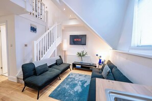 Una sala de estar moderna con una escalera, un televisor de pantalla plana y un comedor.