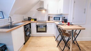 A compact kitchen with a washing machine, microwave, and a dining area with chairs. - Elegant Cardiff Bay Flat Spacious & Comfortable (Cardiff)