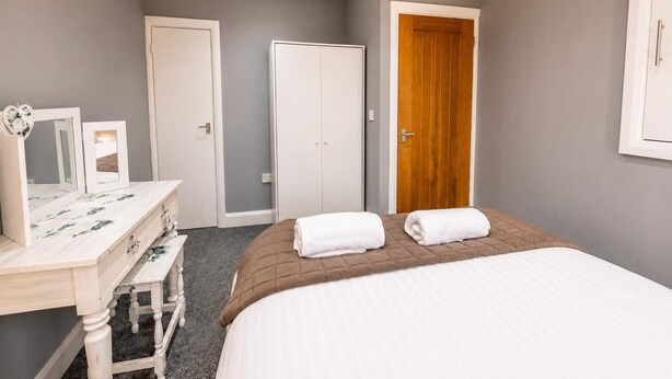 Quarto com cama, penteadeira, espelho e porta.