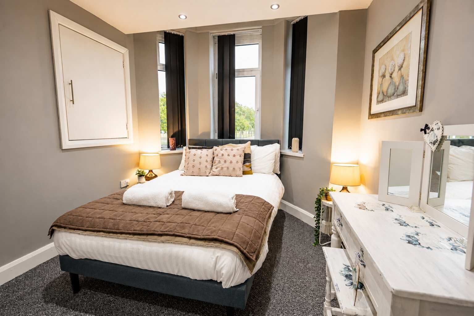 A bedroom with a bed, bedside tables, a dresser, a window, and a framed picture on the wall.