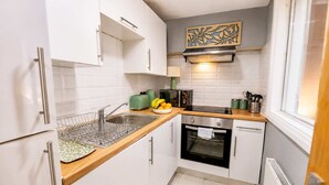Uma cozinha compacta com armários brancos, uma pia de aço inoxidável, um micro-ondas e um forno pequeno.