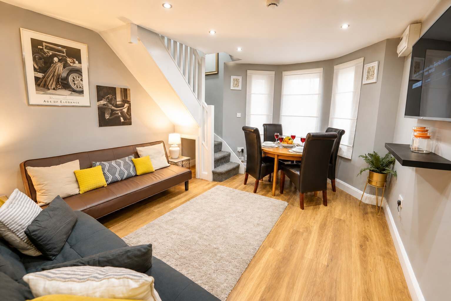 Ein modernes Wohnzimmer mit Sofa, Esstisch, Stühlen, einer Treppe und Kunstwerken an den Wänden.