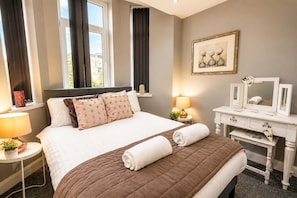 A hotel room with a bed, bedside lamps, a dresser, and a window with curtains.