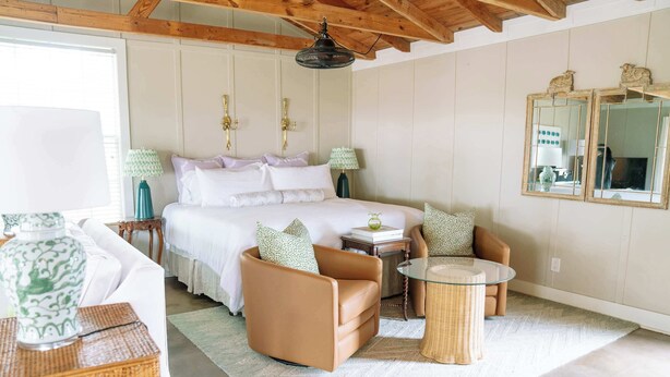 Une chambre à coucher avec un lit, deux chaises, une petite table, un miroir et une fenêtre.