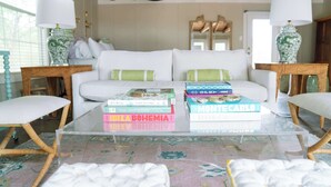 Un salon comprenant un canapé, deux tables d’appoint, une table basse en verre avec des livres et un tapis à motifs.