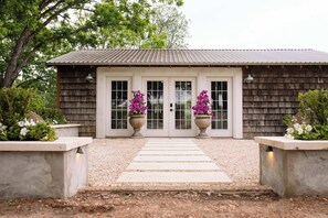 A rustic building with a wooden exterior, a metal roof, and a gravel pathway leading to a set of double doors. - Little Nantucket | Charming Studio Cottage Near RT (Fayetteville)
