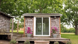 Une structure en bois dotée d’un porche, d’une porte-fenêtre coulissante et de plantes en pot.