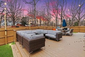 Eine Terrasse mit einer Eckcouch, einem Esstisch, Stühlen und einem blauen Sonnenschirm.