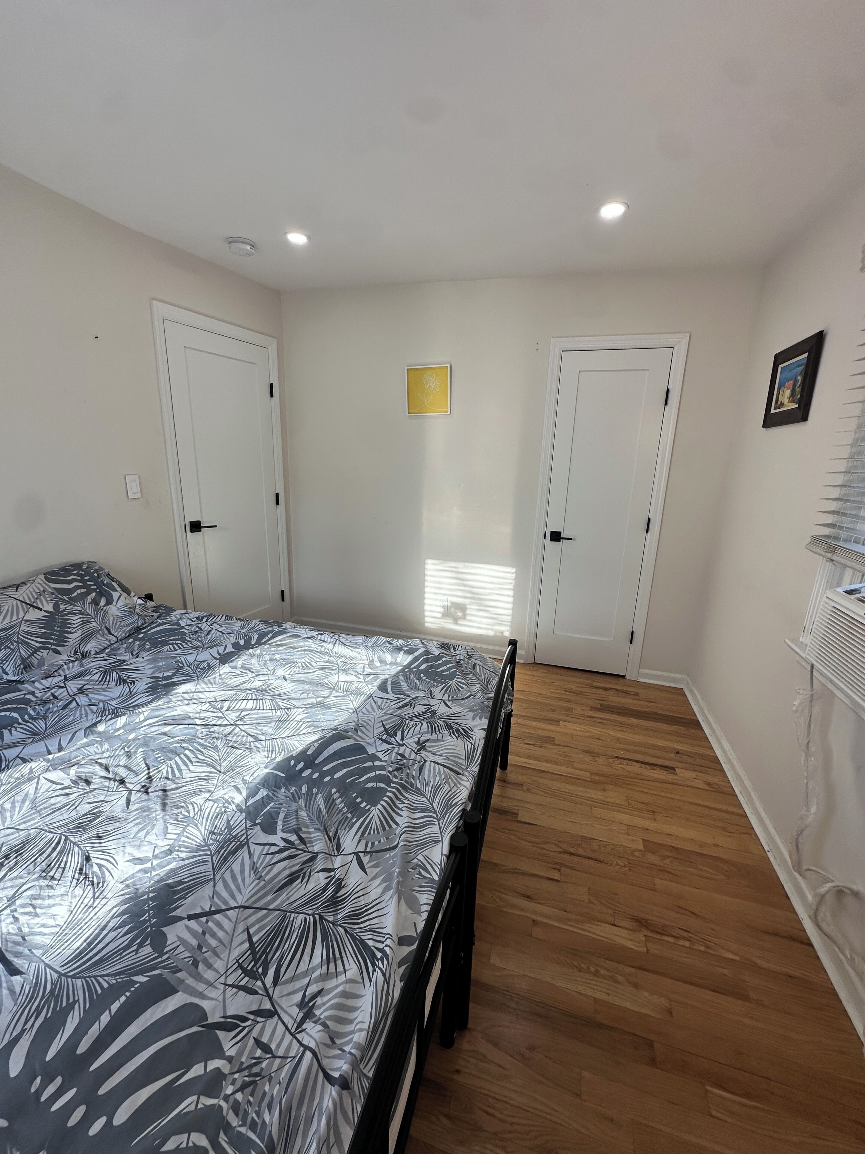 A bedroom with a bed, two doors, a window, and a radiator.