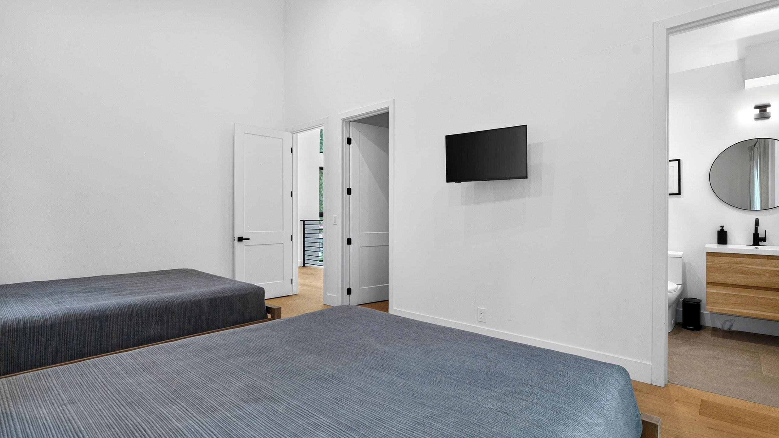 Un dormitorio con dos camas, televisión, espejo y baño con inodoro y lavamanos.