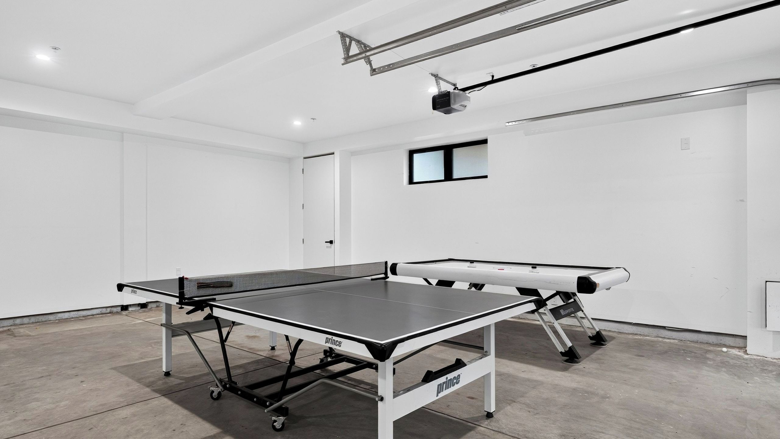Una mesa de ping pong con ruedas en una habitación con paredes blancas y un proyector instalado en el techo.