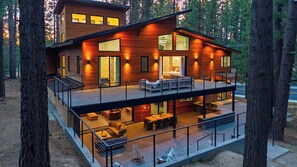 Ein modernes, zweistöckiges Haus mit Balkon, Sitzgelegenheit im Freien und Blick auf den umliegenden Wald.