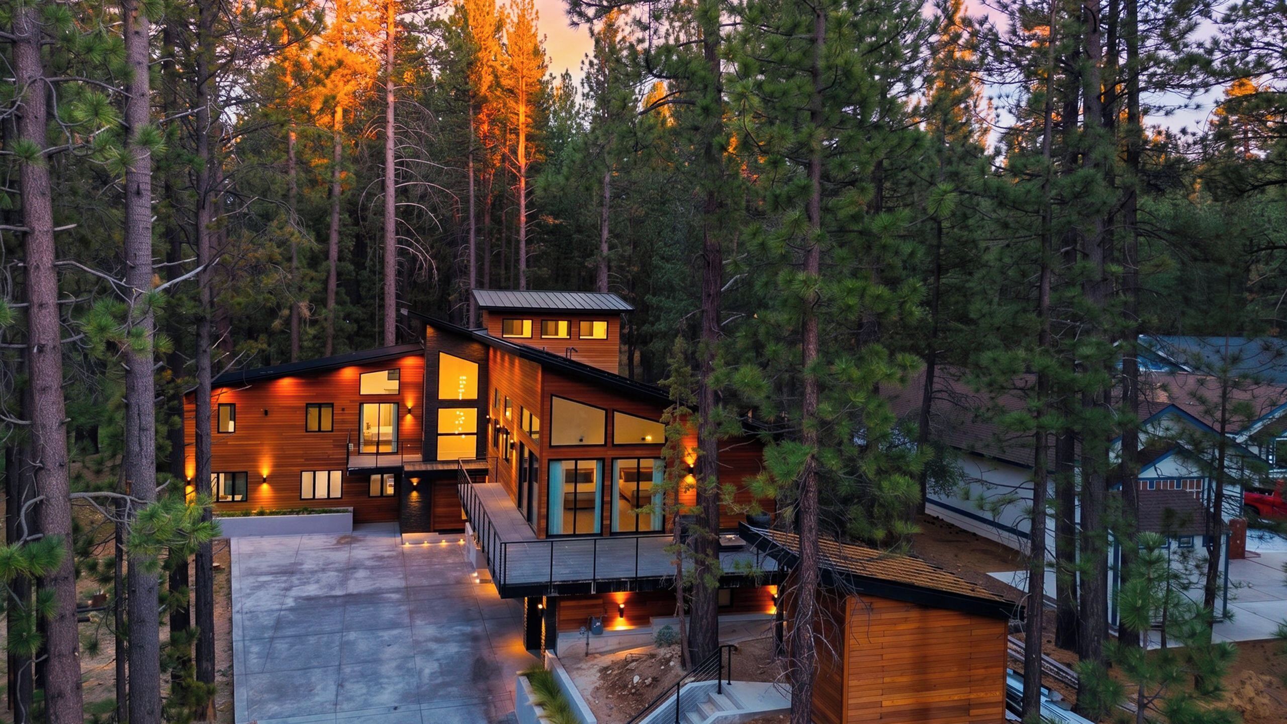 Une cabane moderne en bois, entourée de grands pins, dotée d’une vaste terrasse et de grandes fenêtres.