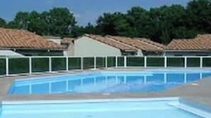 A swimming pool with a tiled deck, surrounded by a white fence and trees in the background.