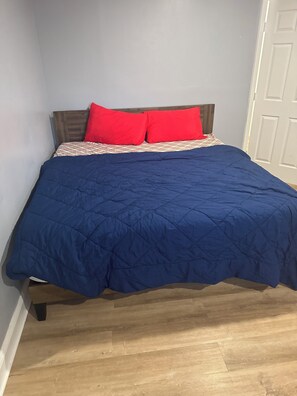 A bed with a blue quilt, two red pillows, and a patterned bedspread. -  1  bedroom in a basement with share bathroom and share kitchen (Waldorf)