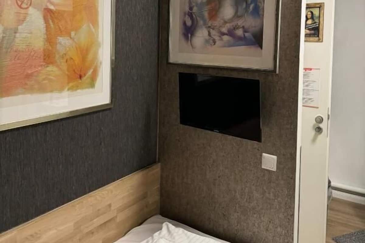 A hotel room with a bed, a large abstract painting on the wall, and a smaller framed picture above the bed.