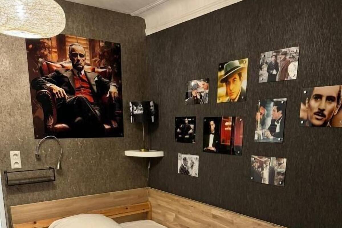 A bedroom with a wooden bed, a wall-mounted lamp, and a series of framed pictures.