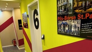 A hallway with a bright yellow wall, a red and yellow striped pattern, and a door marked with the number 6. - Room-Pauli (Hamburg)