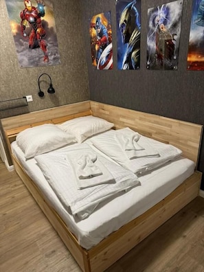 Una cama de madera con sábanas blancas, una lámpara de pared y carteles de superhéroes.