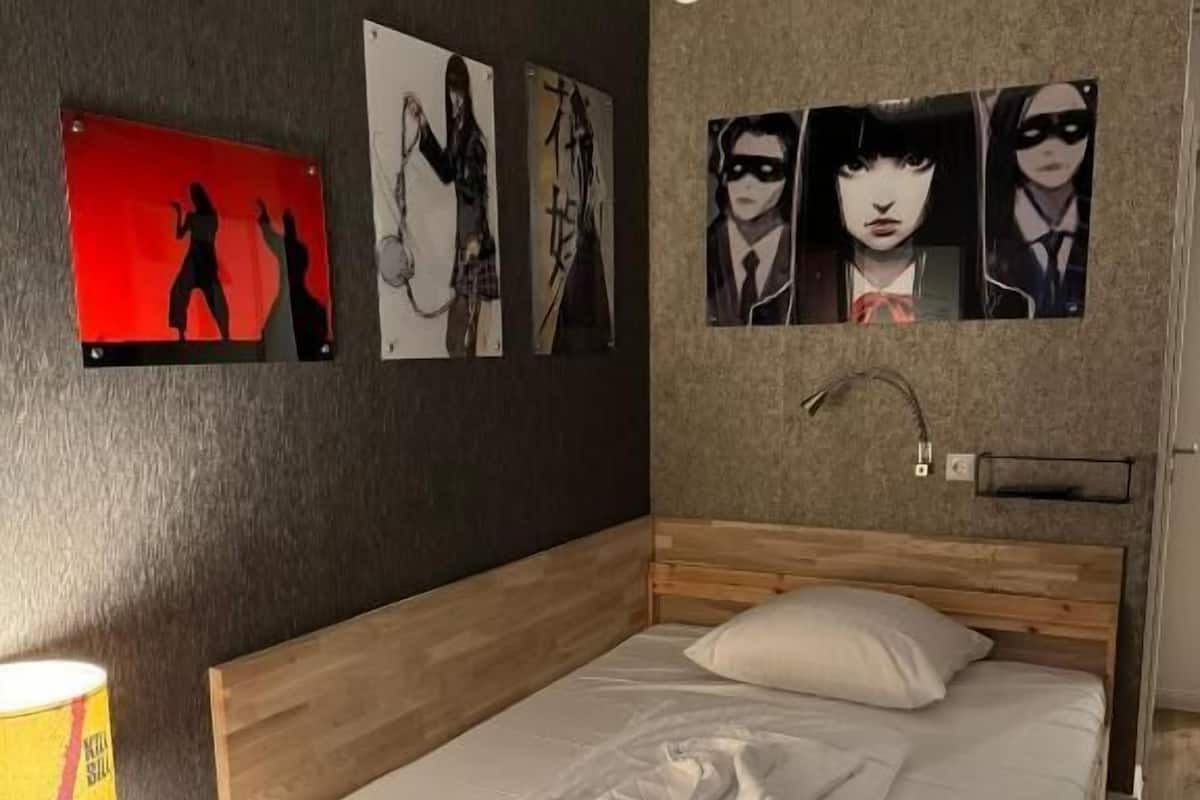 A single-bed room with a wooden headboard, a bedside table with a lamp, and wall art.