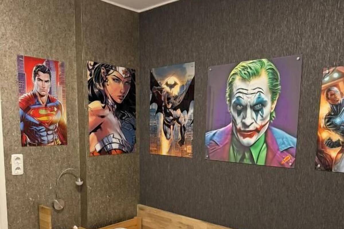 A bedroom with a bed, a wall-mounted shelf, and four superhero posters.