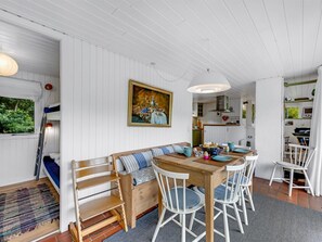 Una habitación acogedora con un banco de madera, una mesa de comedor con sillas, un cuadro en la pared y un ventanal con vistas al verdor.