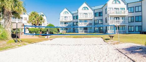 A beachfront hotel with multiple-story buildings, a sandy beach in the foreground, and a clear blue sky.