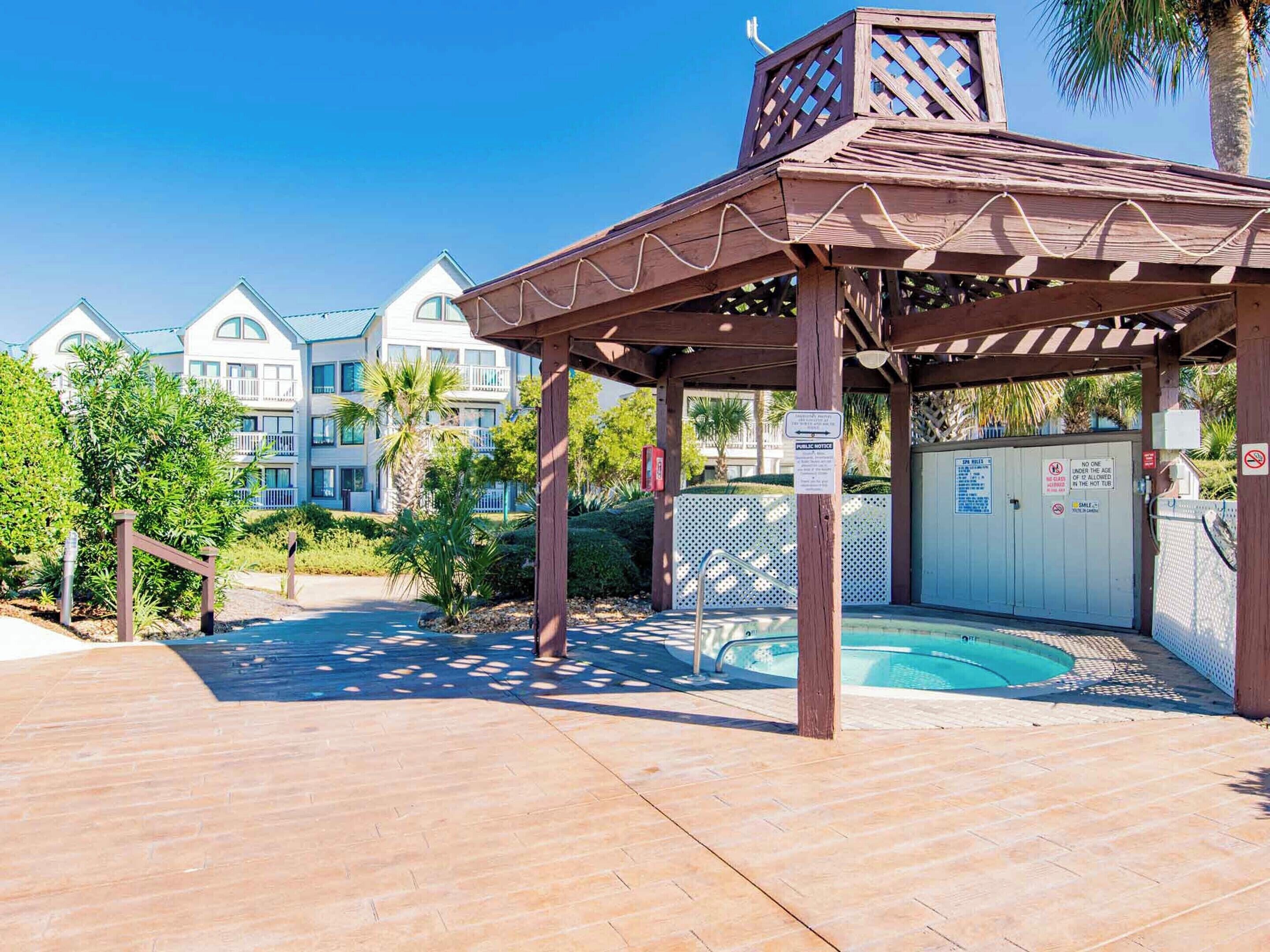 A covered outdoor area with a pool, wooden pergola, and a gated entrance.