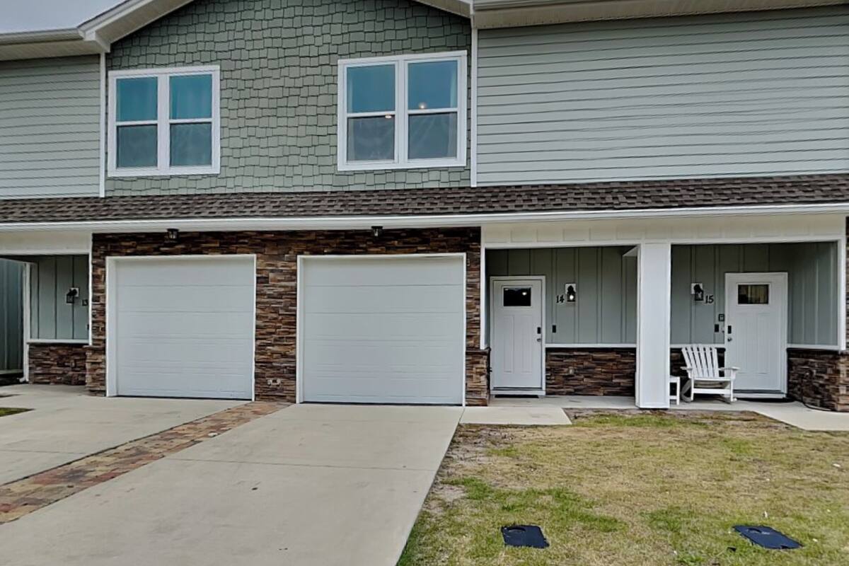 A two-story house with two garage doors, a stone facade, and a covered porch with a chair.