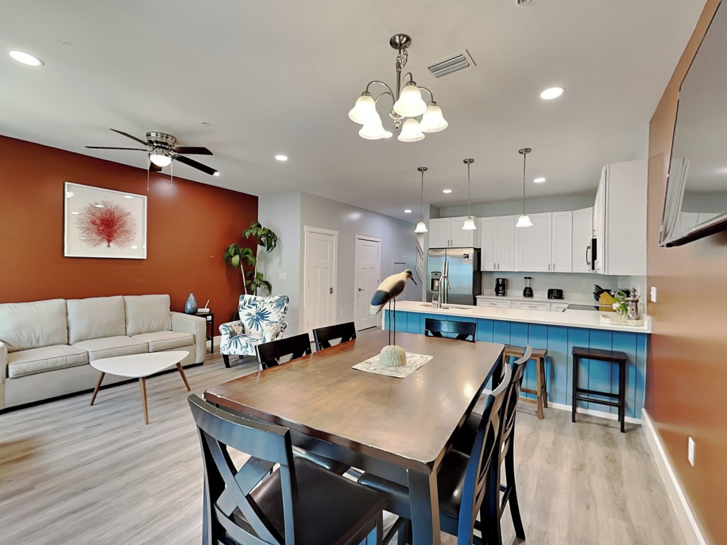 Una cocina moderna con armarios blancos, una isla central y una zona de comedor con una mesa y sillas de madera.