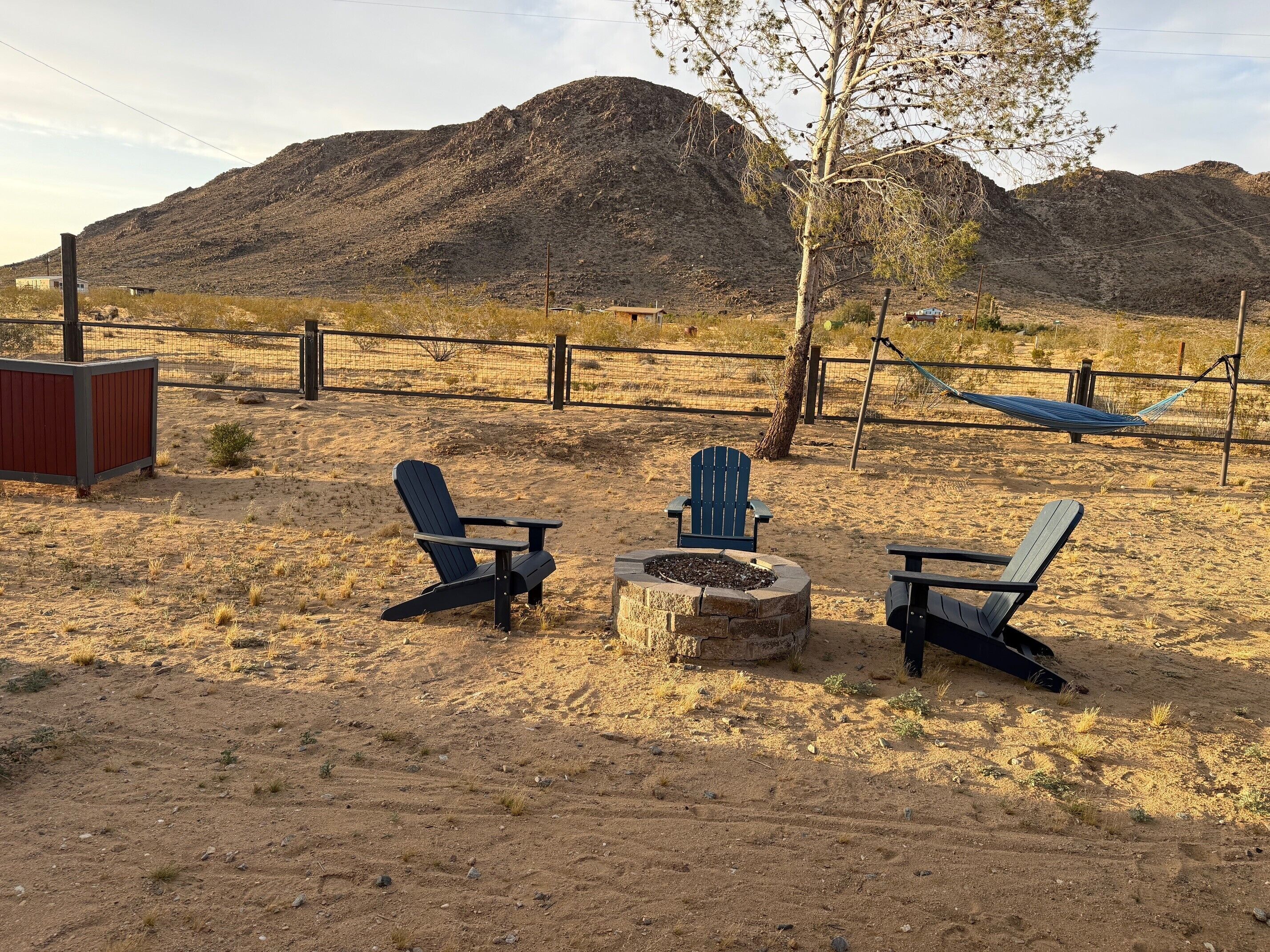 A desert landscape with a fire pit, two Adirondack chairs, and a hammock.