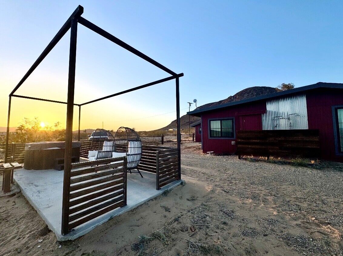 A metal structure with a bench and a table, a red building with a window, and a clear sky.