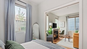 A modern hotel room with a bed, a television, a fireplace, and a view of the outdoors. - Nob Hill Stay, Reserved Garage Parking, Fireplace, Ground Floor Apartment (Portland)