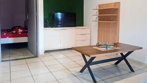 A room with a bed, a television on a white cabinet, a wooden table with a glass object, and a green wall. - THE MILANOSIMPLY (Kourou)