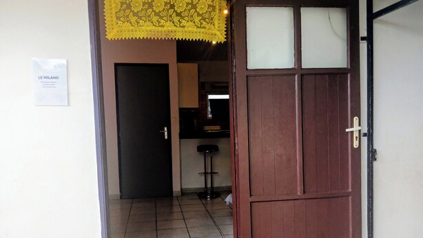 A doorway leading to a room with a tiled floor, a black door, and a yellow decorative item above the door. - THE MILANOSIMPLY (Kourou)