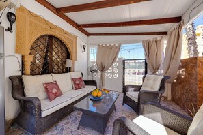 Eine überdachte Terrasse mit Korbmöbeln, einem Glastisch und einem dekorativen Bogen.
