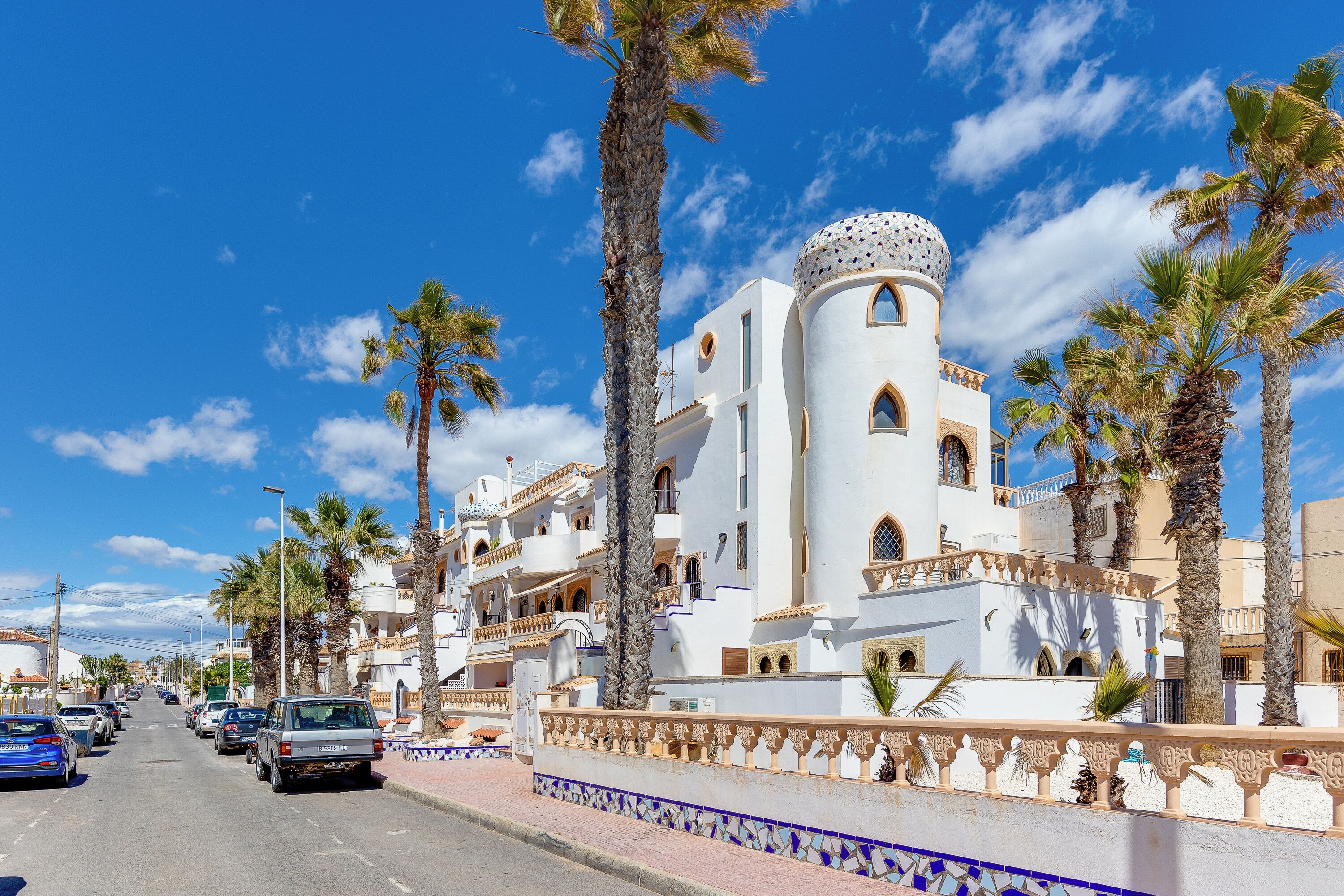 A street lined with palm trees and white buildings with balconies.