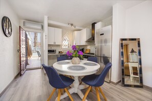 Eine moderne Küche mit weißen Schränken, einem Edelstahlkühlschrank und einem Essbereich mit rundem Tisch und blauen Stühlen.