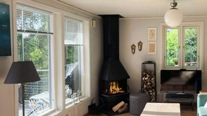 Ein Zimmer mit Kamin, einem Tisch, einer Lampe und großen Fenstern.