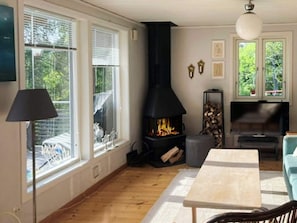 Ein Zimmer mit Kamin, einem Tisch, einer Lampe und großen Fenstern.