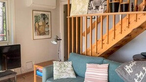 Ein Wohnzimmer mit einer Couch, einem Fernseher, einer Lampe und einer Treppe.