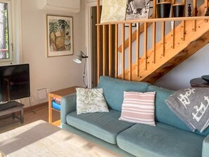 Ein Wohnzimmer mit einer Couch, einem Fernseher, einer Lampe und einer Treppe.