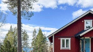 Eine rote Holzhütte mit Tür und Fenstern, umgeben von Bäumen und einer grünen Wiese.